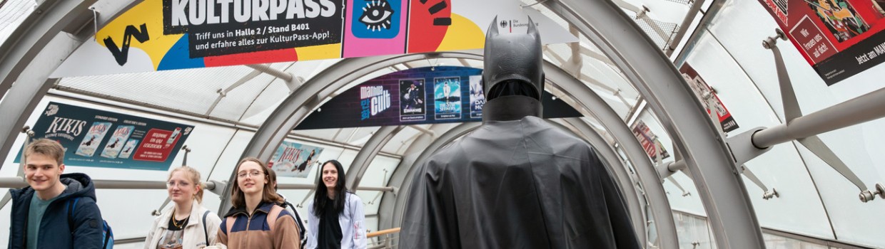 Eine als Batman verkleidete Person läuft über die Manga-Comic-Con, andere Besucher:innen schauen interessiert