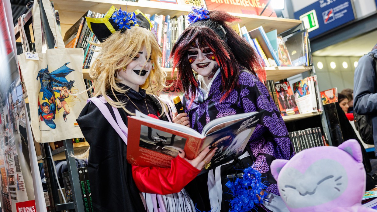 2 Cosplayer:innen lesen in einem Buch an einem Messestand auf der Manga-Comic-Con 2024
