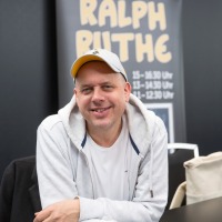 Ralph Rute sitze an einem Signiertisch auf der Manga-Comic-Con 2024 und lächelt in die Kamera Ralph Rute sitze an einem Signiertisch auf der Manga-Comic-Con 2024 und lächelt in die Kamera