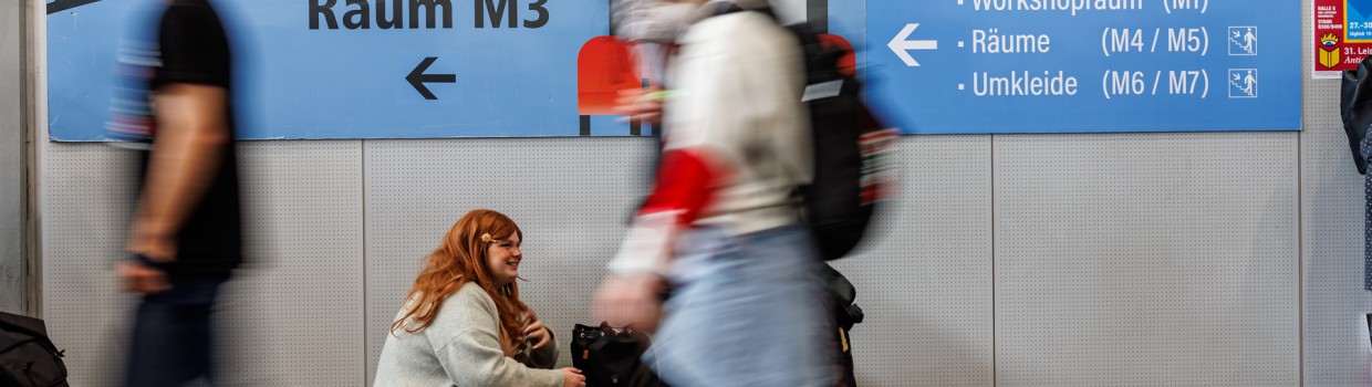 blaues Wegweiserschild zum Anime Kino auf der Manga-Comic-Con 2025 mit vorbeilaufenden Personen