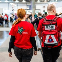 Two members of the Awareness Team SAM from the Manga Comic Con 2025 are walking through the exhibition hall.
