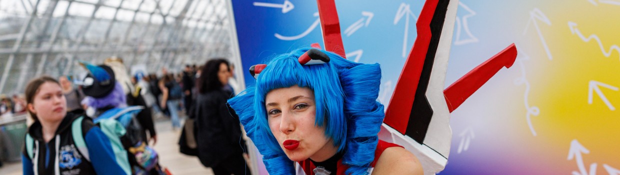 The mascot of the Manga Comic Con, Macoco, is blowing a kiss in front of a colorful backdrop at the Manga Comic Con 2025.
