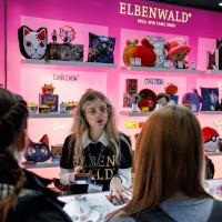 Vendor at the Elbenwald booth at the Manga Comic Con 2025, surrounded by colorful anime and manga merchandise.
