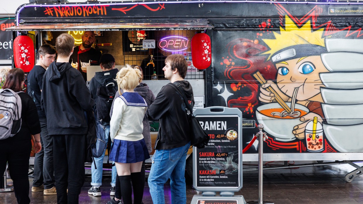 Mehrere Personen stehen vor einem Food Truck in der Schlange auf der Manga Comic Con 2025. Der Food Truck ist beschriftet mit "Naruto kocht" und trägt eine Zeichnung von einer Nudeln-essenden Mangafigur.