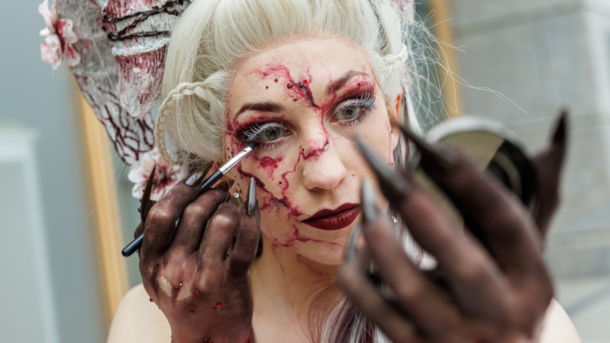 Close-up of a cosplayer applying a false eyelash to her eye.