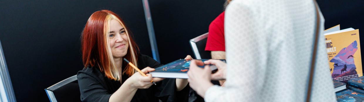 Jenny Jinya überreicht einem Fan ein signiertes Buch auf der Manga-Comic-Con 2025 Jenny Jinya überreicht einem Fan ein signiertes Buch auf der Manga-Comic-Con 2025